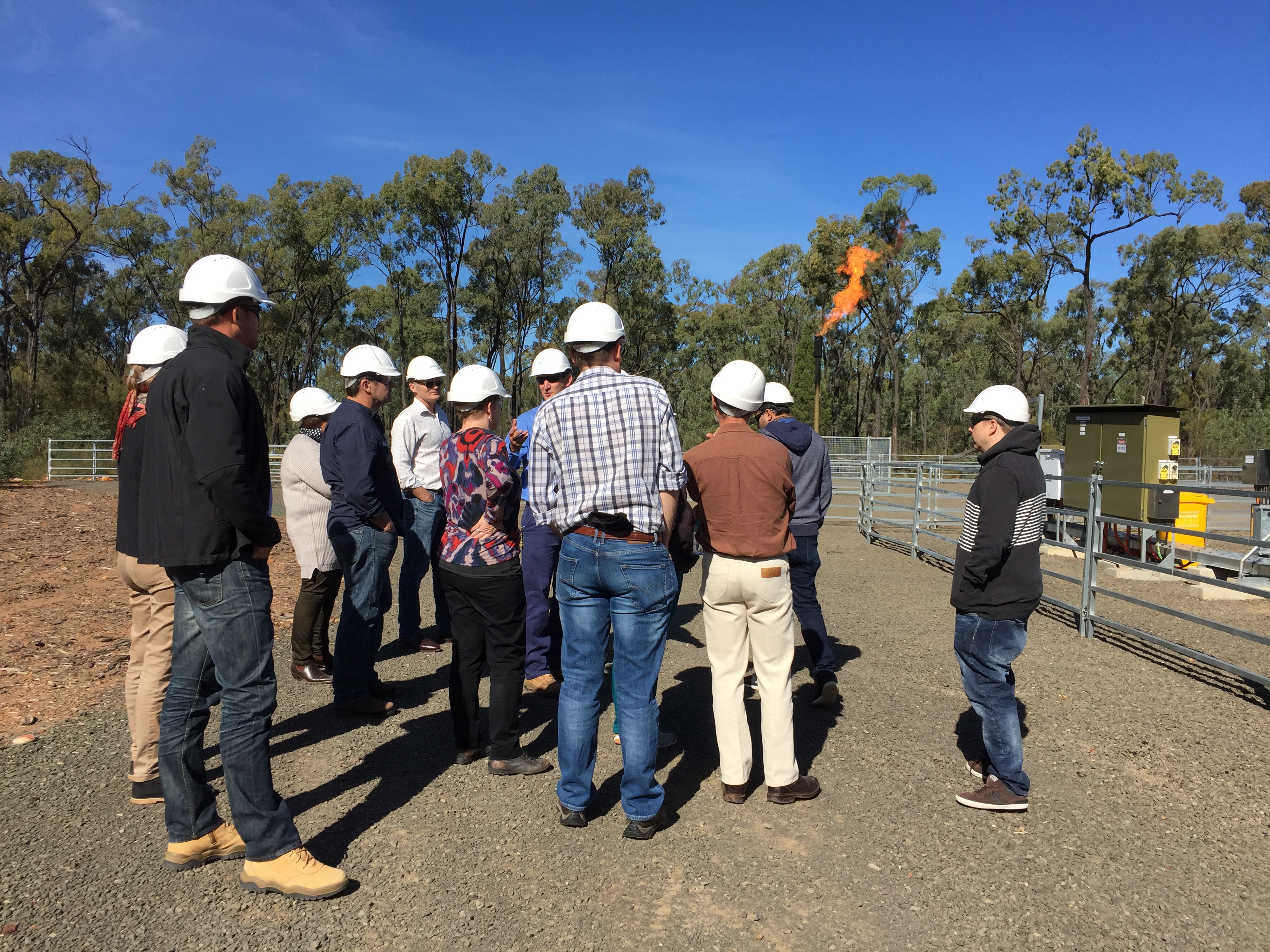Group of people in hard hats standing near coal seam gas well