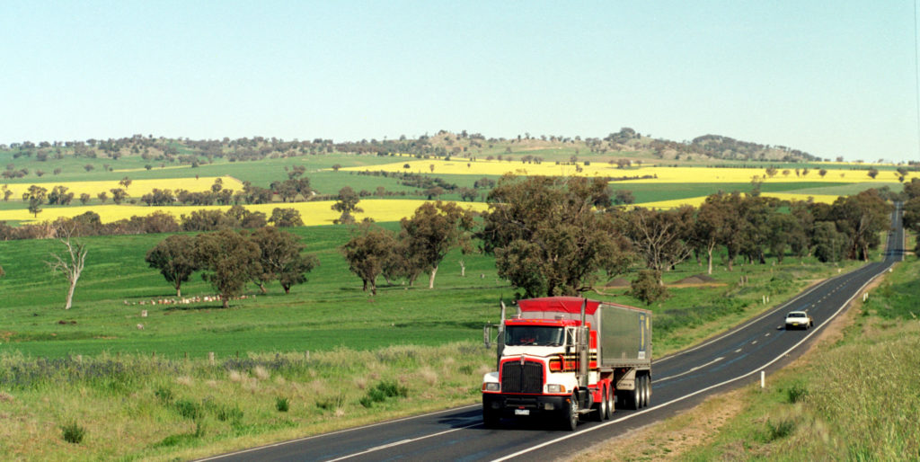 Truck on highway, near Cowra, NSW, with Canola and wheat fields in the background.